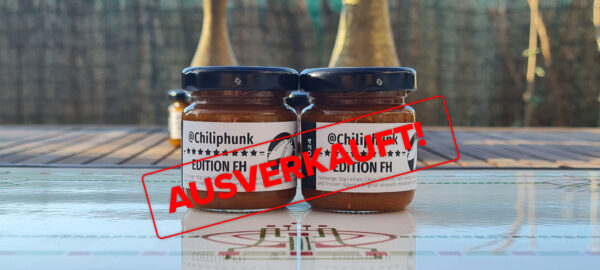 Label mit dem Text "Ausverkauft" liegt über dem Bild. Das Bild: 2 Gläser "Chiliphunk Edition FH" Chilipaste auf einem Holztisch; Dahinter ist unscharf der Gartenzaun und Messingvasen am Tisch.